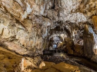 Interior da Caverna do Diabo mostrando imensas colunas calcíticas e diversas formações rochosas iluminadas, criando um ambiente místico e espetacular.