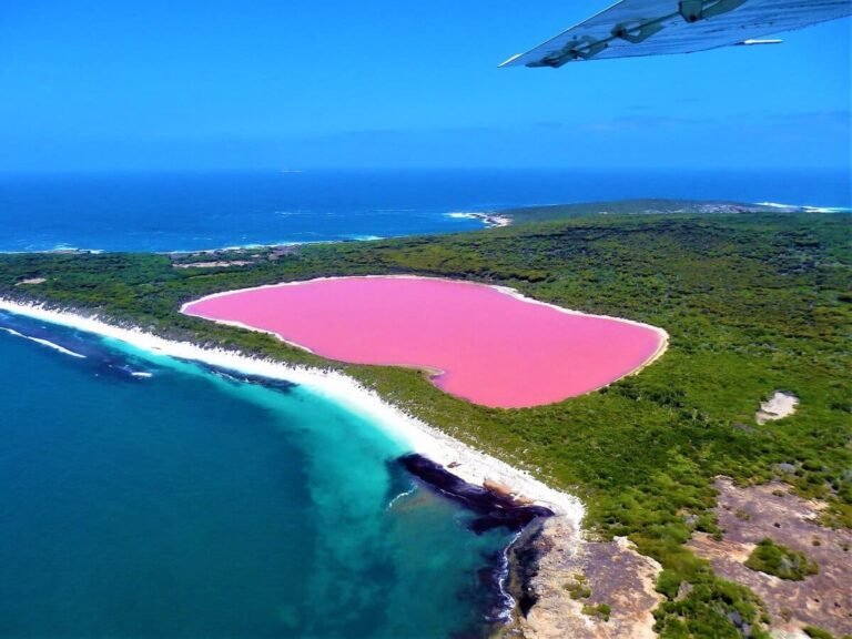 Vista aérea vibrante do Lago Hillier, destacando sua impressionante cor rosa contrastando com o azul do oceano circundante na Austrália Ocidental.