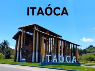 Portão de entrada para Itaoca, destacando o pórtico com o nome da cidade, cercado por exuberante vegetação verde, simbolizando o convite ao ecoturismo na região.